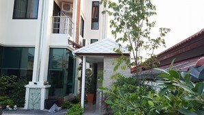 Un edificio moderno con fachada de vidrio, una pequeña entrada cubierta y un jardín con diversas plantas.
