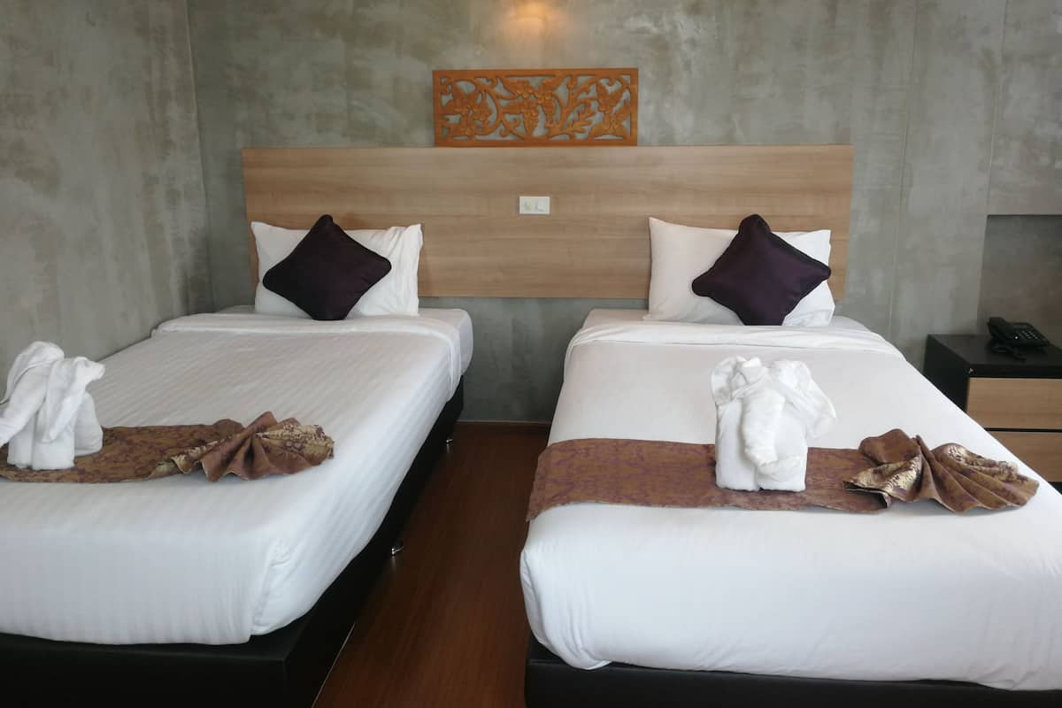 Dos camas juntas con ropa blanca, mantas marrones claras y oscuras, y almohadas decorativas.
