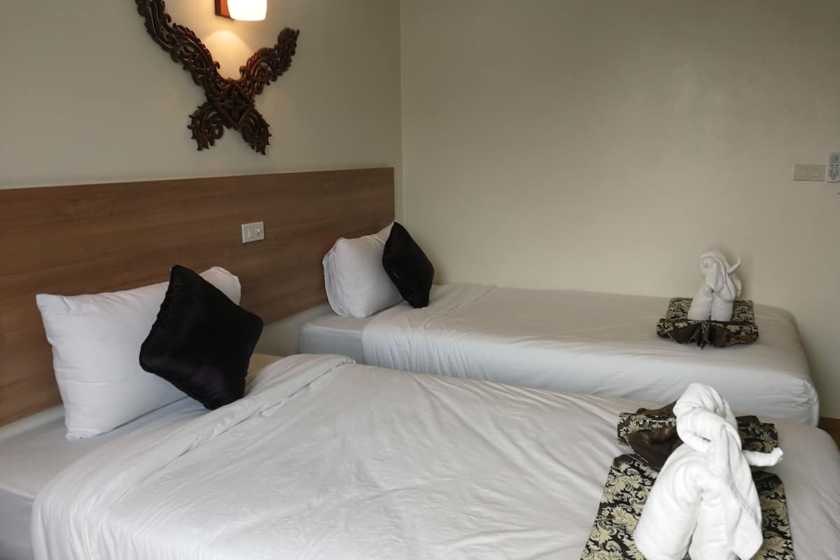 Habitación de hotel con dos camas individuales, cada una con ropa de cama blanca y almohadas negras. Se observa una pieza decorativa en la pared sobre las camas y una pequeña estatua en la mesita de noche.