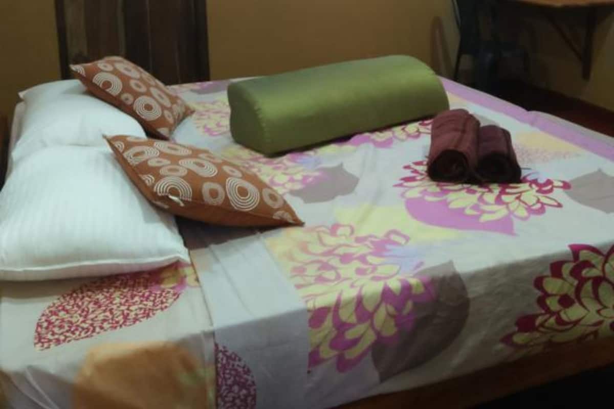 Uma cama de solteiro com colcha estampada, um travesseiro verde e vários travesseiros decorativos.