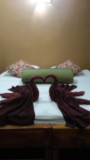 A bed with a green pillow, two brown towels arranged in a heart shape, and patterned pillows. - khaya villa (Habarana)
