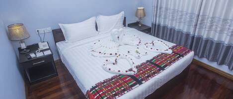 A neatly made bed with white linens and a decorative swan design on the bedspread. There are two bedside tables with lamps and a phone. The room has wooden flooring and light blue walls.
