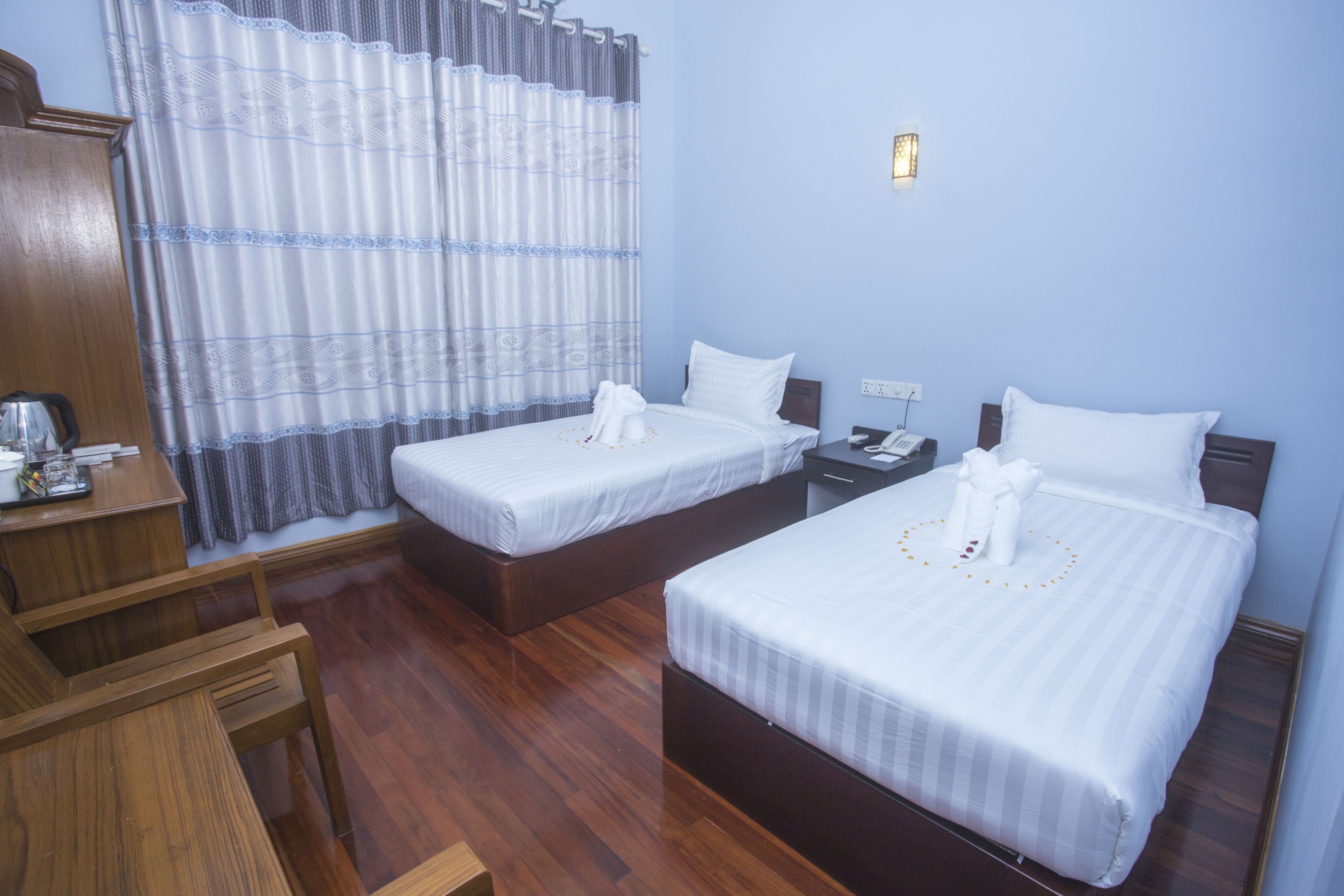 A hotel room with two single beds, wooden furniture, a desk, and a nightstand.