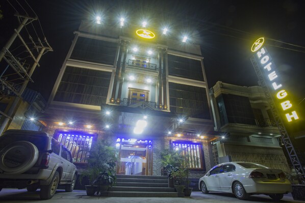 A hotel entrance with a prominent sign, a staircase leading to the door, and two parked cars.