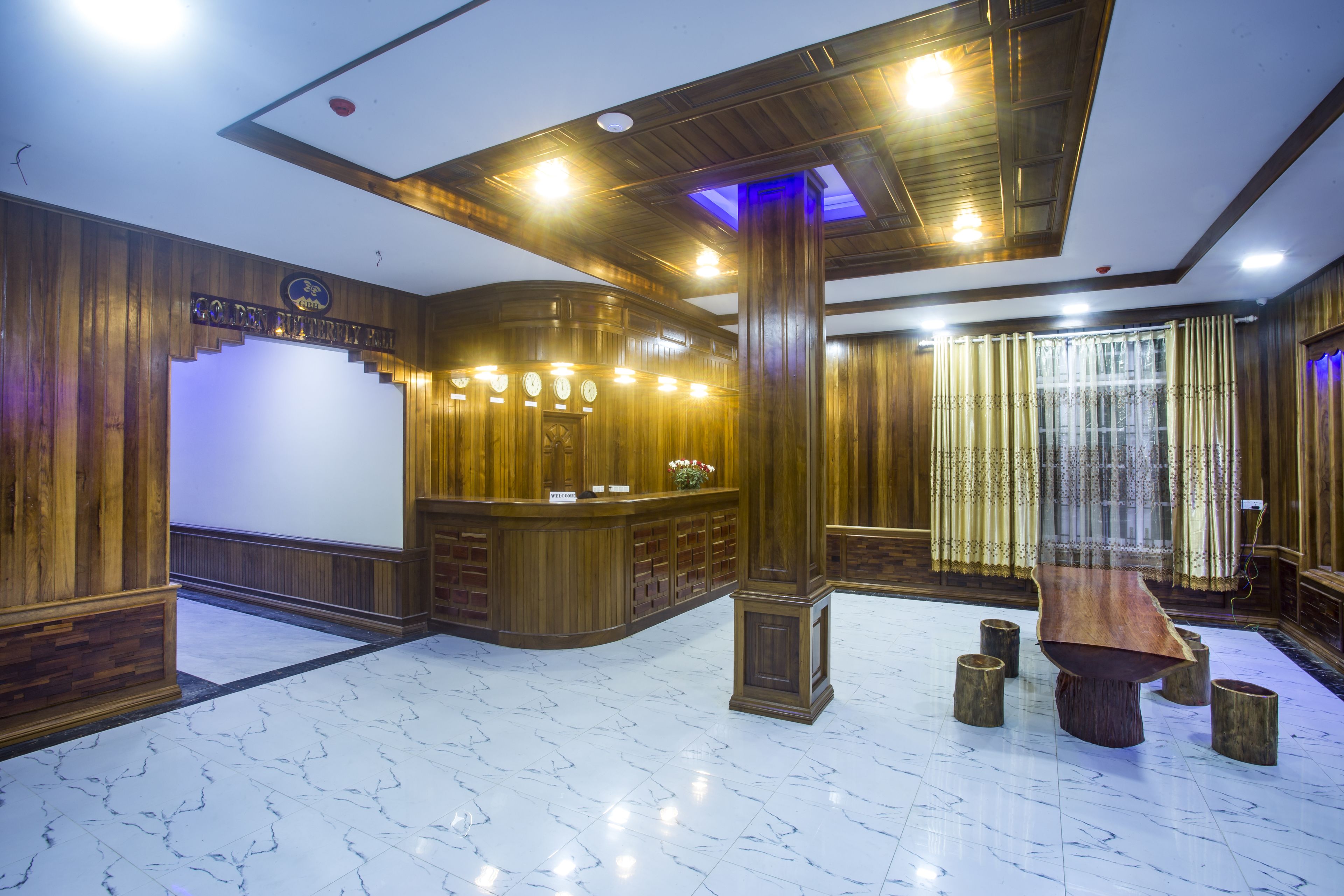 A reception area with a wooden reception desk, a marble floor, and a large wooden table with stools.