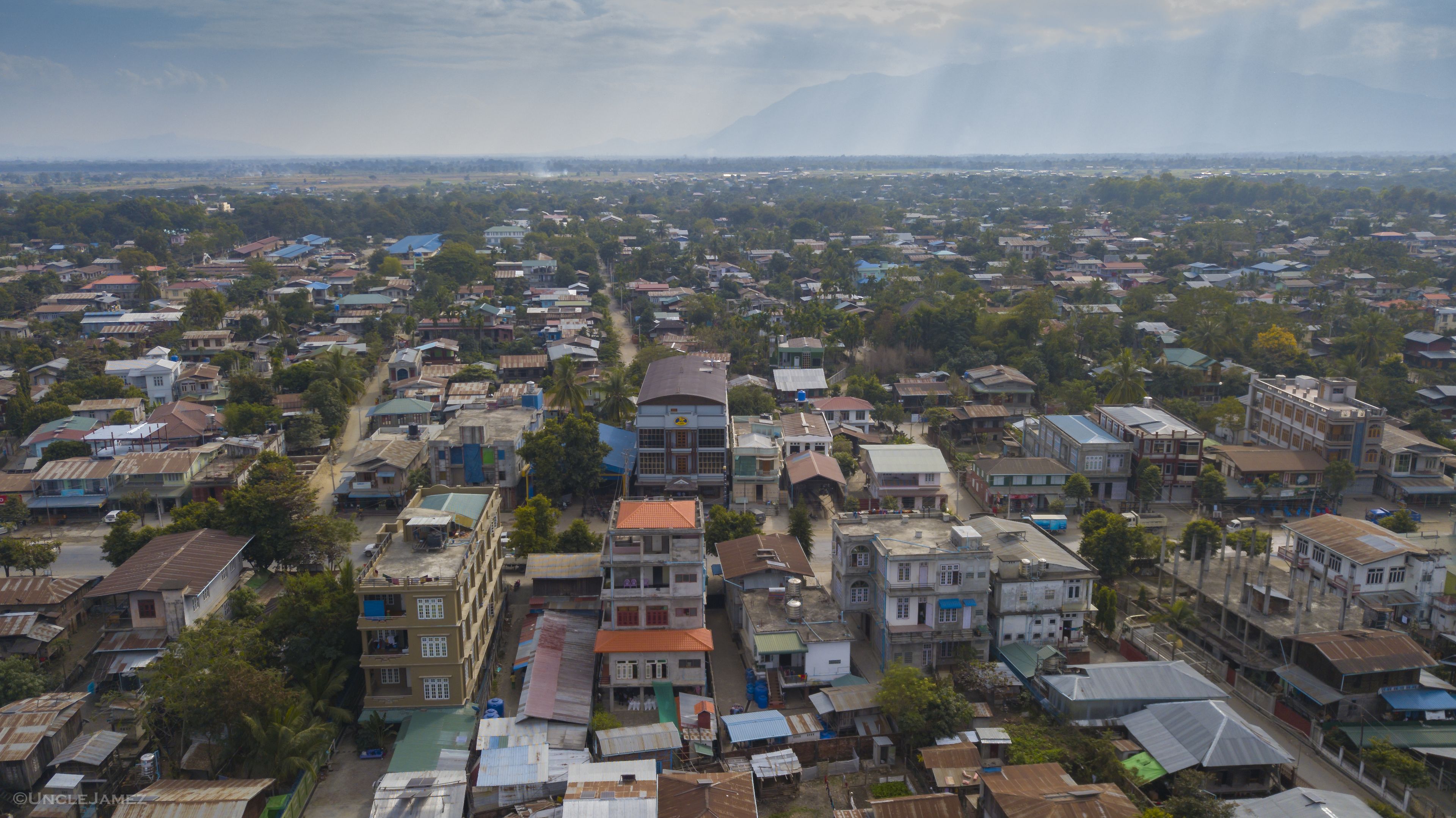 A densely packed urban area with various buildings, including multi-story structures and single-story houses, under a cloudy sky.