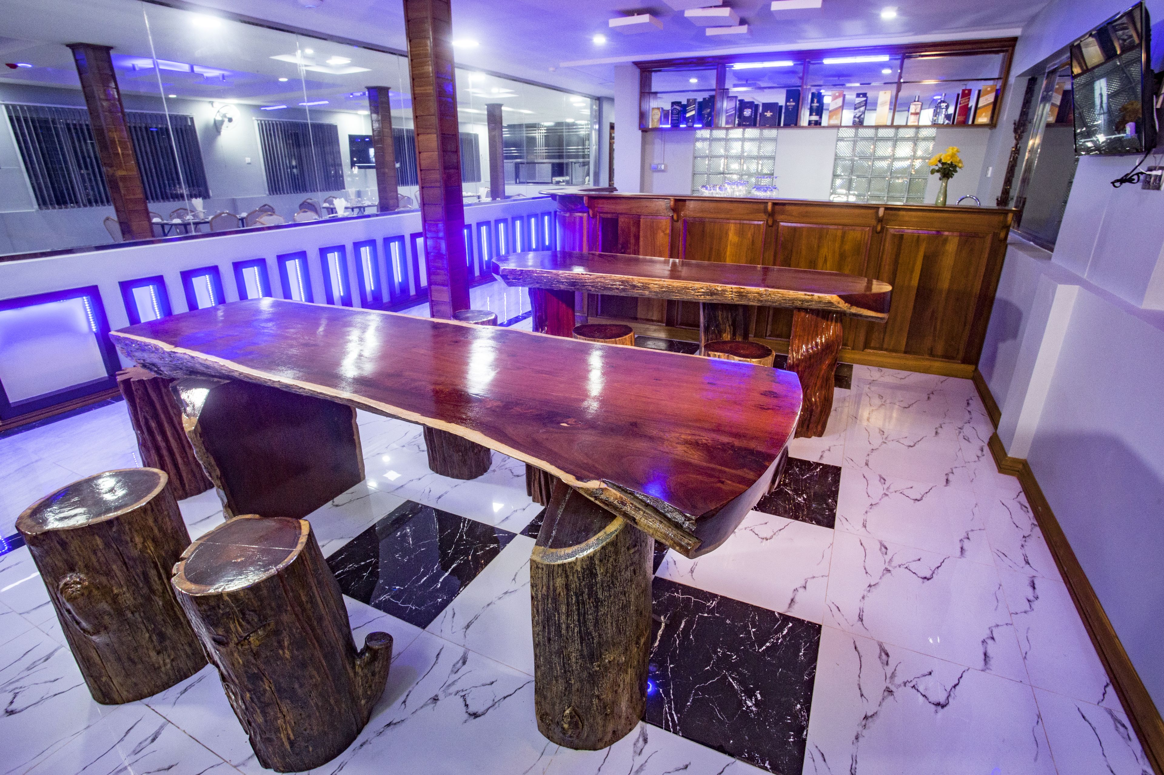 Zona de bar con una barra de madera larga, taburetes y piso de baldosas de mármol.