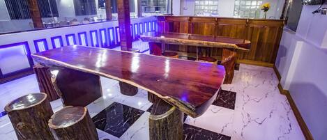 Zona de bar con una barra de madera larga, taburetes y piso de baldosas de mármol.