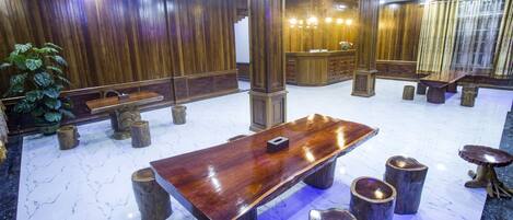 Un amplio vestíbulo con un gran mostrador de recepción de madera, suelo de mármol y una mesa de madera central rodeada de taburetes.