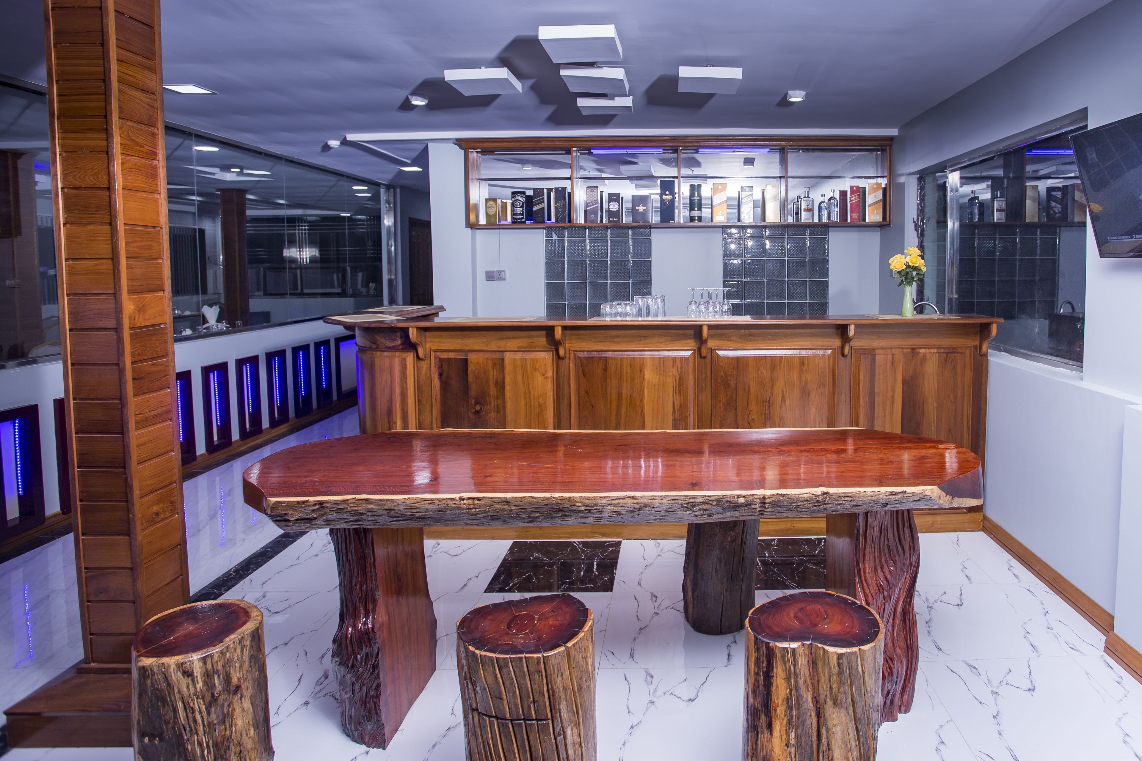 A modern bar area with a wooden bar counter, stools, and a large mirror above the counter reflecting the bar area.