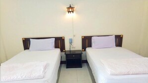 Habitación de hotel con dos camas individuales, una mesita de noche entre ellas y una lámpara fijada a la pared.