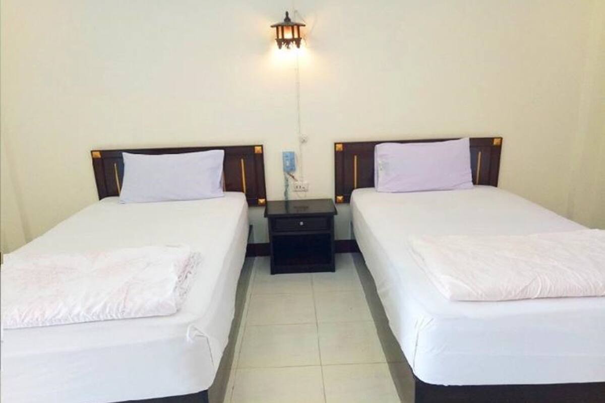 Habitación de hotel con dos camas individuales, una mesita de noche entre ellas y una lámpara fijada a la pared.