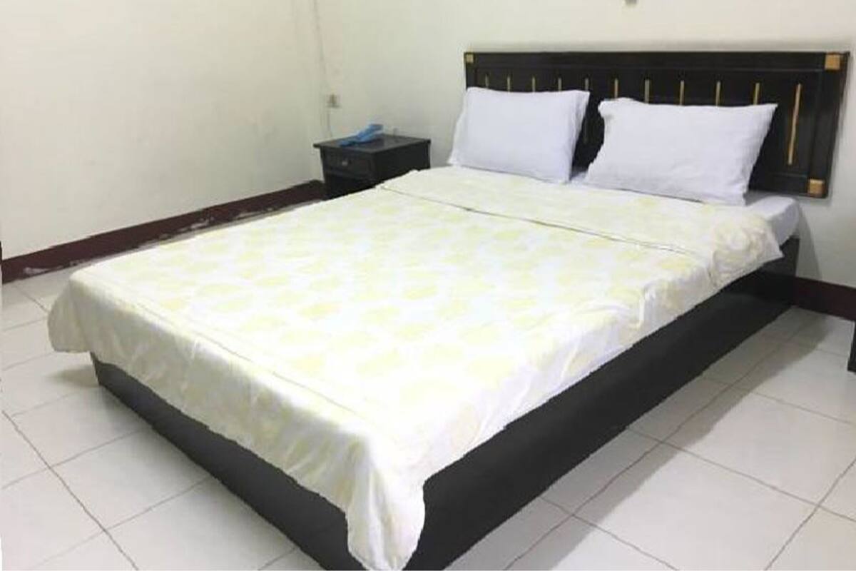Una habitación de hotel estándar con una cama individual, una mesita de noche y una pared lisa.