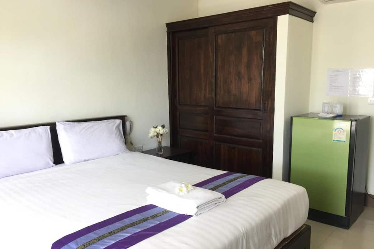 A hotel room with a large bed, a wardrobe, and a small refrigerator.
