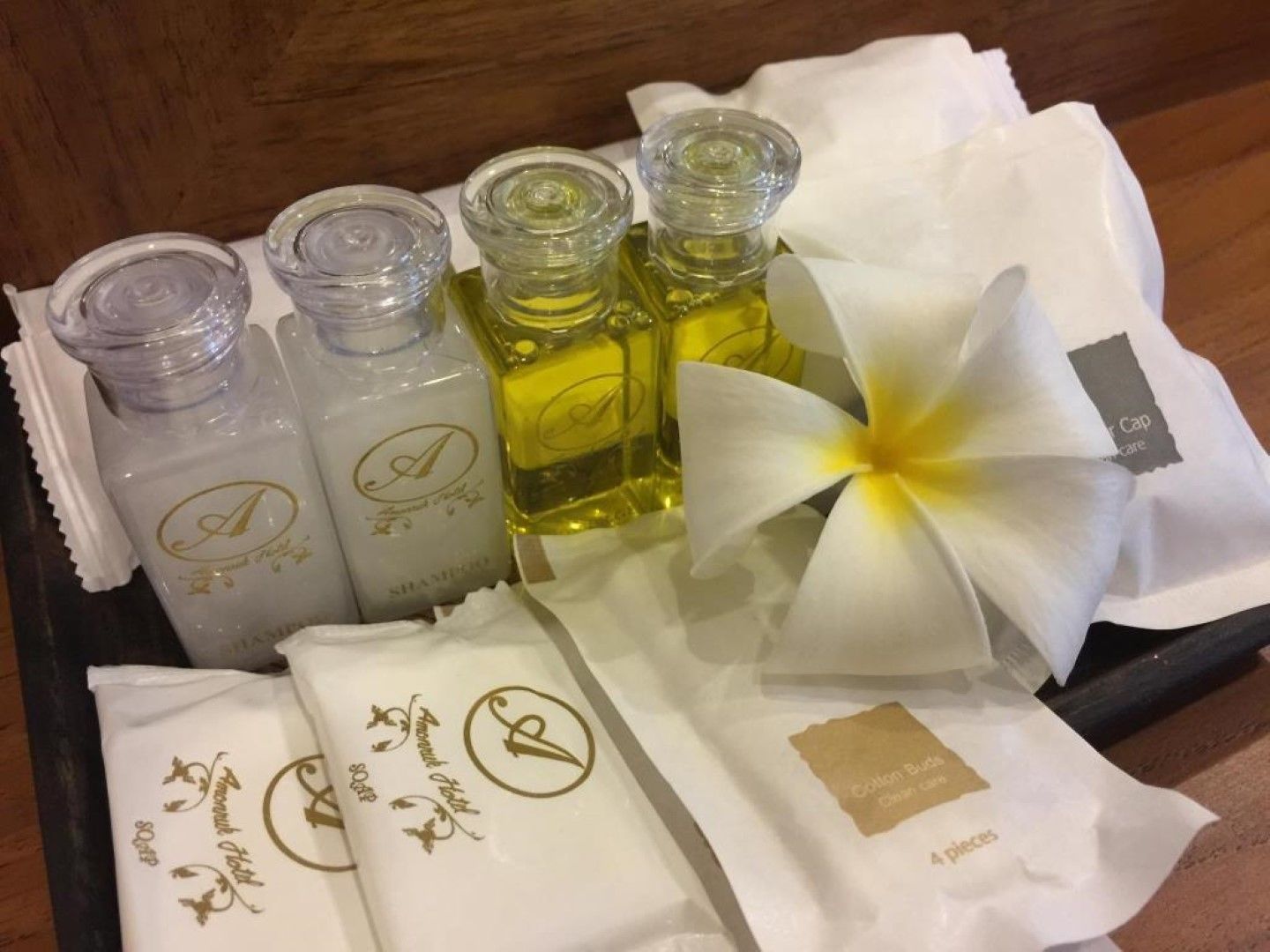 A tray with four bottles of liquid, a white flower, and two white gift bags with gold lettering.