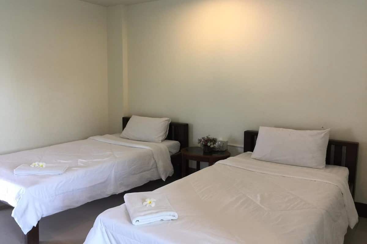 Two single beds with white linens and pillows, a small round table with a vase of flowers, and a wall-mounted light fixture.