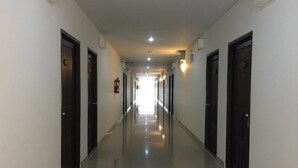 A long, narrow hallway with doors on both sides, a fire extinguisher on the left wall, and a ceiling light. - Amonruk  Hotel 2 (Phrae)