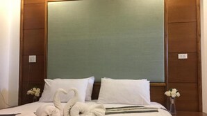 A neatly made bed with two heart-shaped towels, a green headboard, and a small vase with flowers on the nightstand. - Amonruk  Hotel 2 (Phrae)