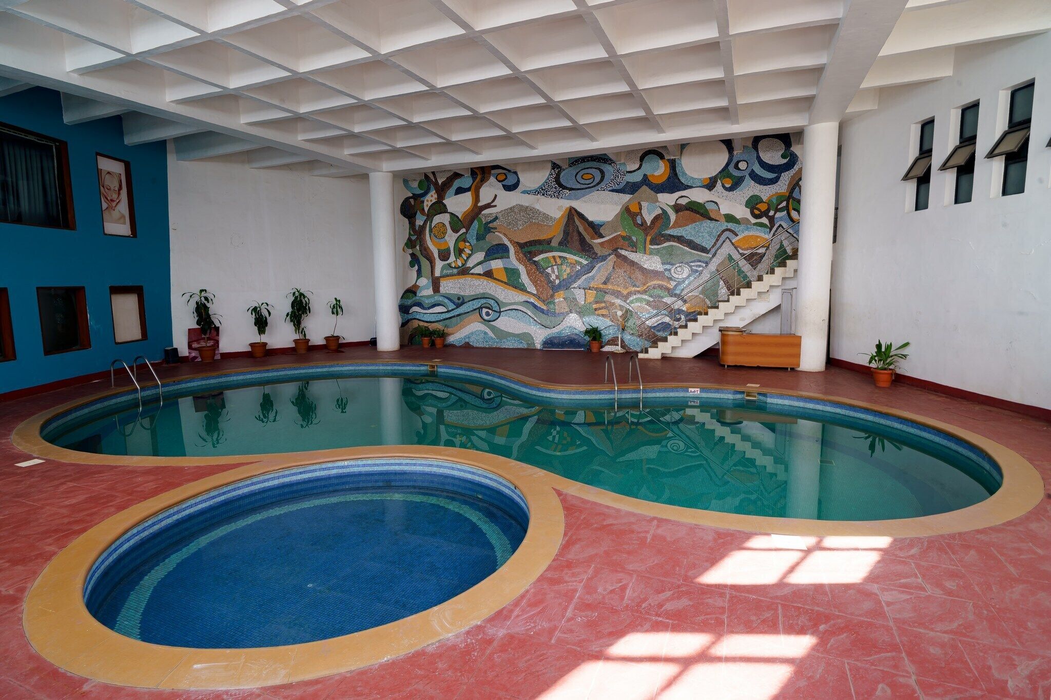 Ein Innenpool mit einem Mosaikbild an der Wand und einer Treppe, die zu einer höheren Ebene führt.