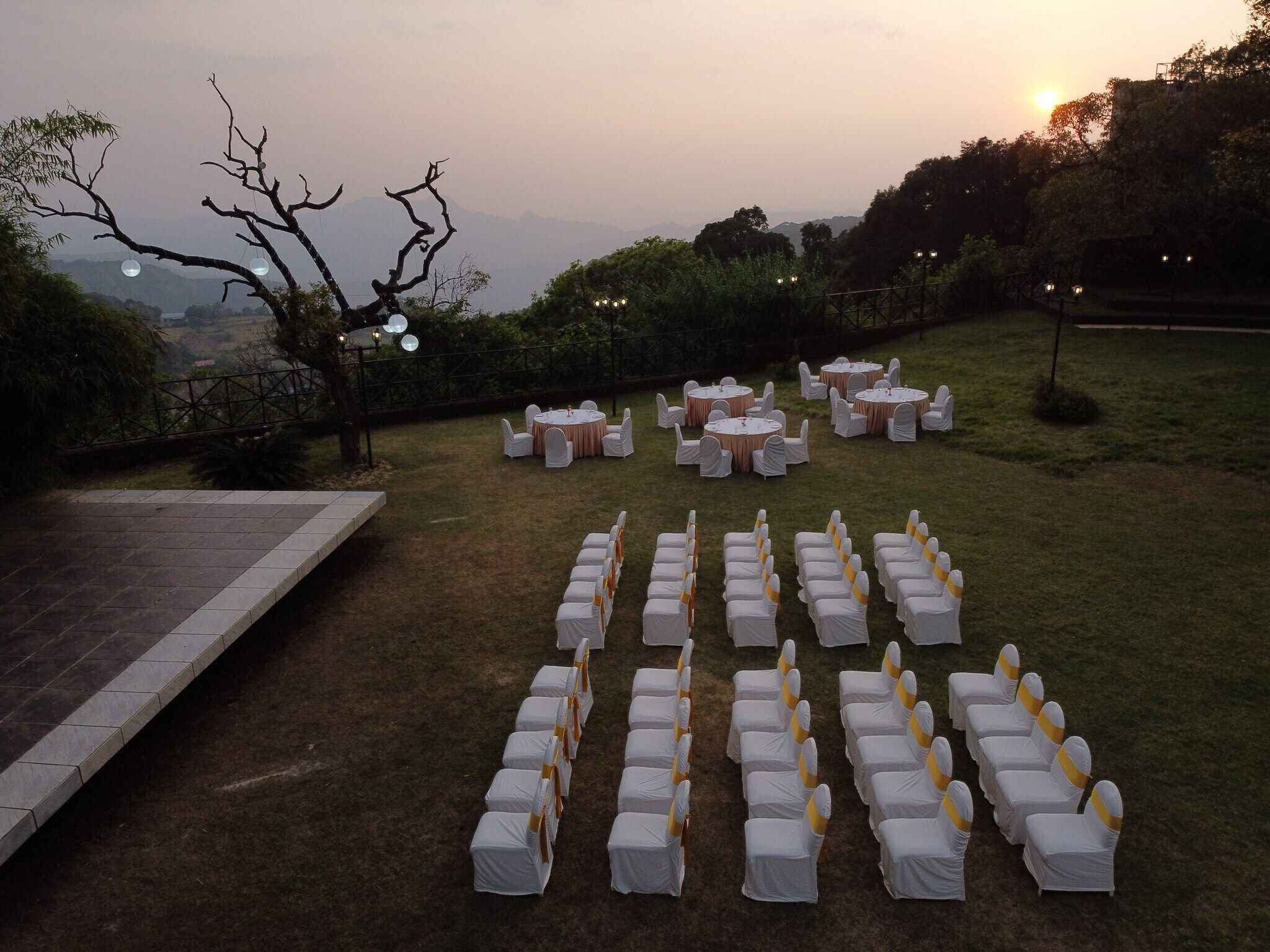 An outdoor wedding setup with round tables and chairs arranged on a grassy lawn, overlooking a scenic landscape.
