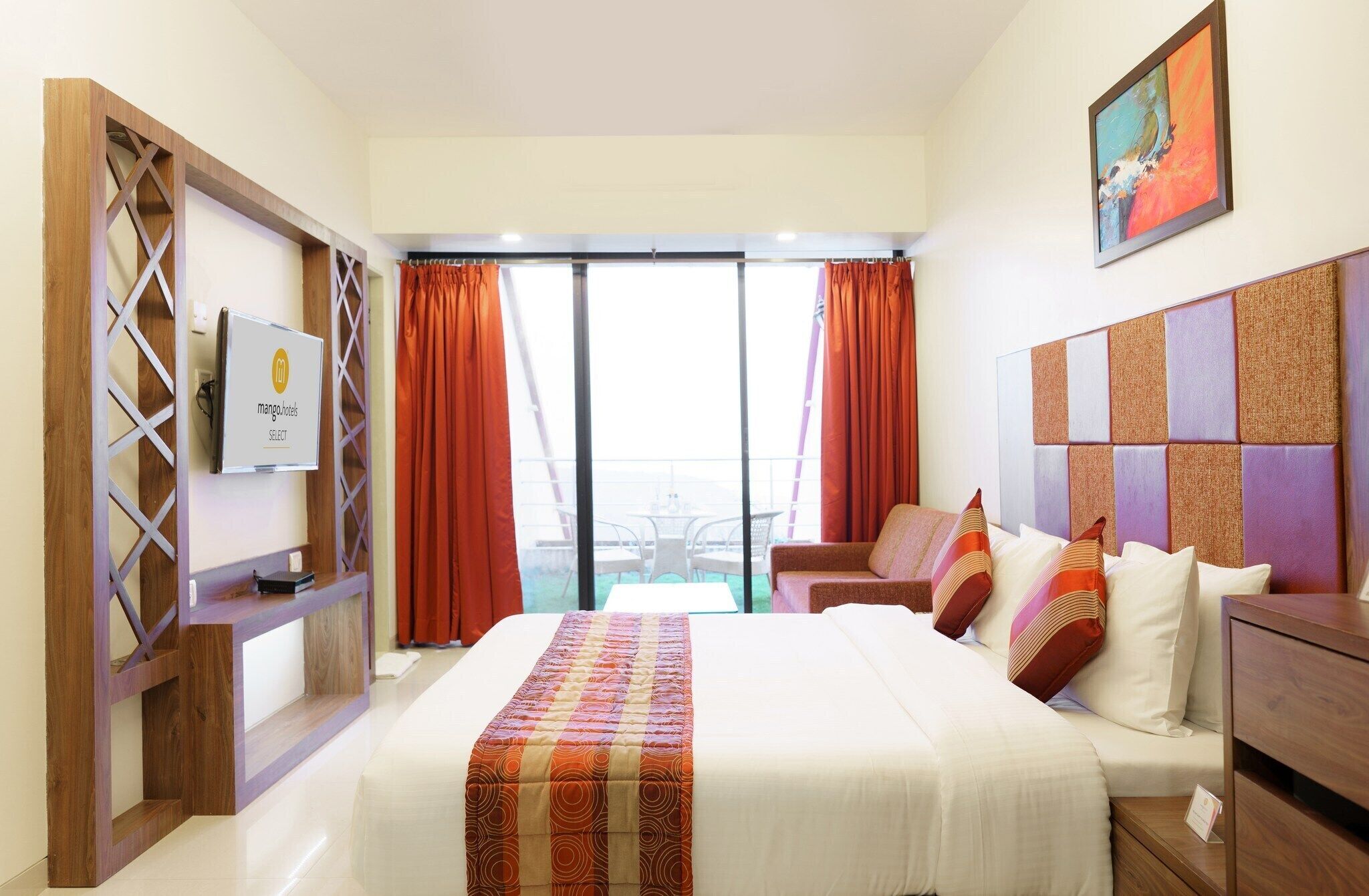 A hotel room with a bed, a desk, a TV, and a balcony with orange curtains.