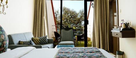A hotel room with a bed, a sofa, a chair, and a balcony with curtains.