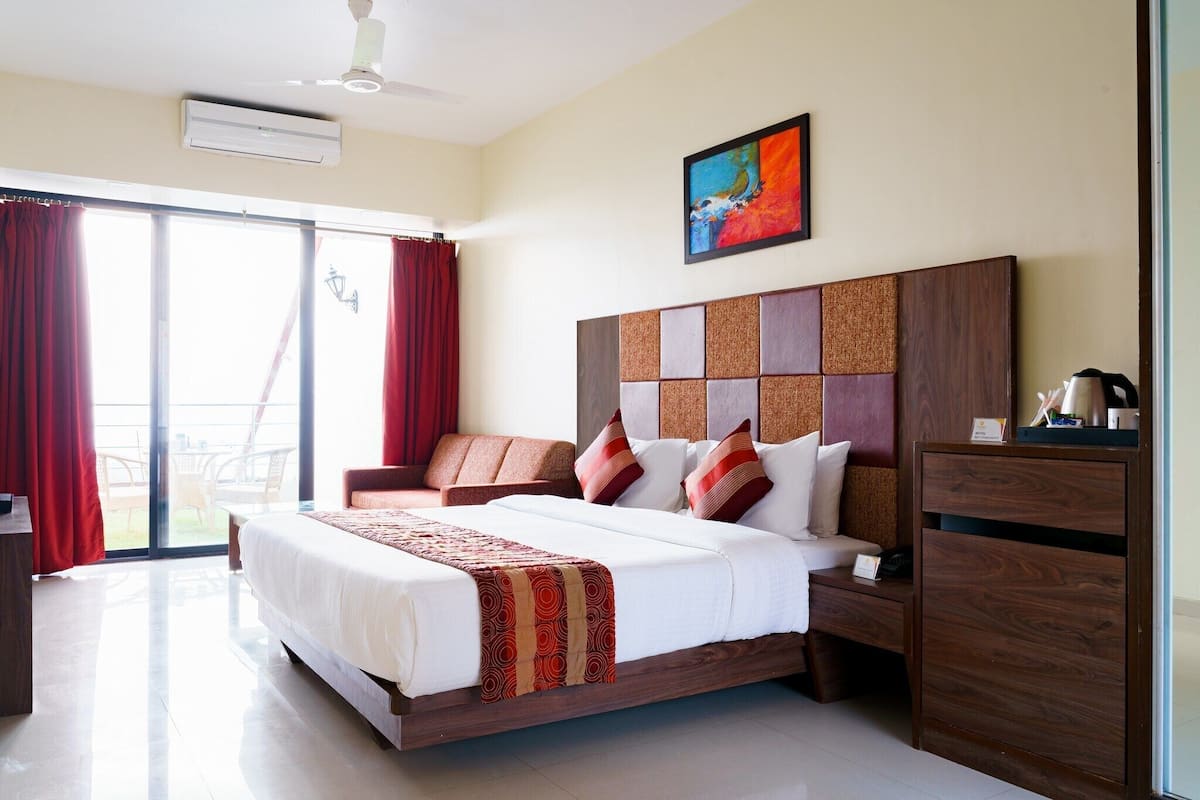 A hotel room with a large bed, a wooden headboard, a desk, and a view of the outdoors.