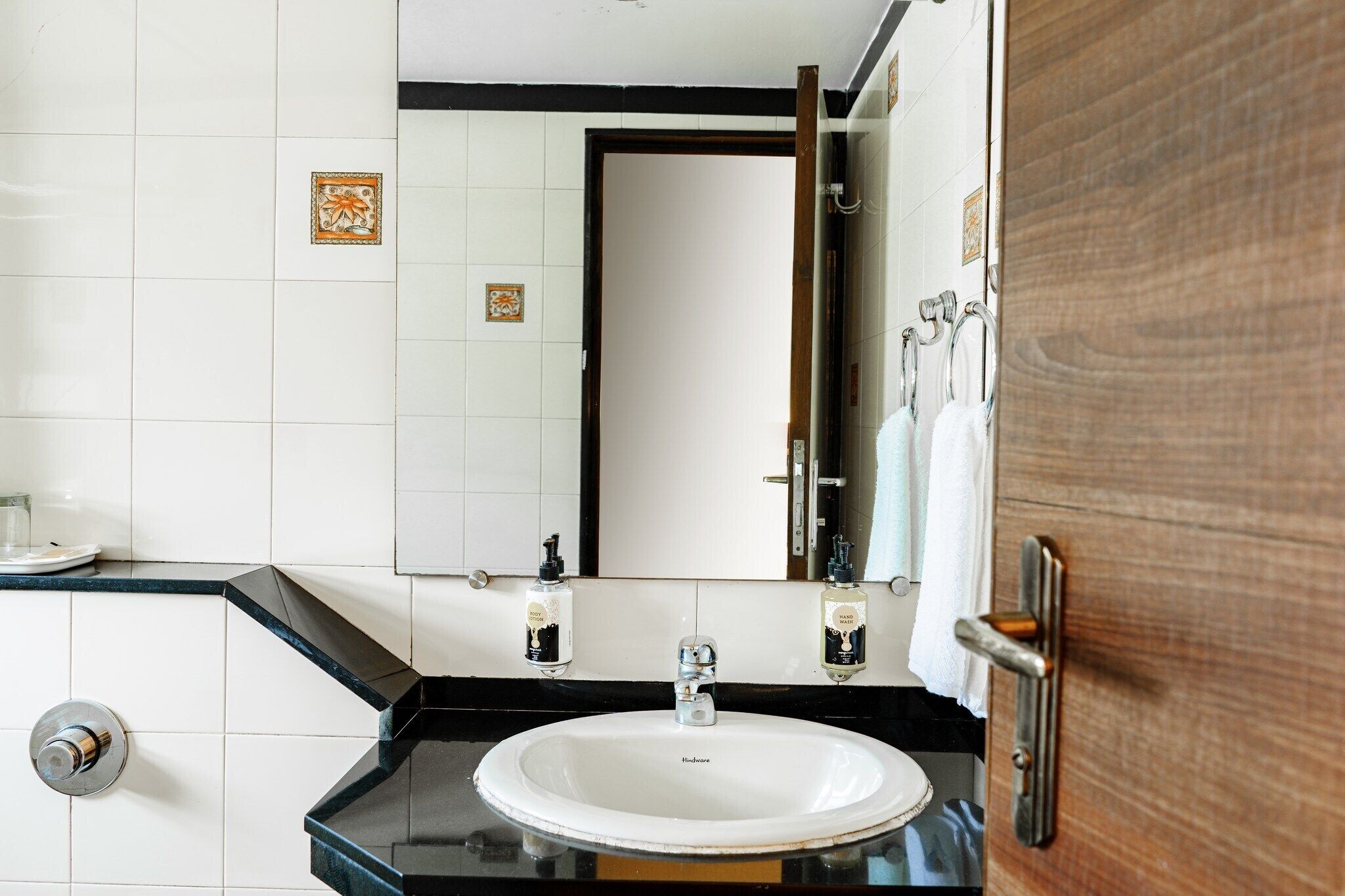 Un baño con lavamanos blanco, encimera negra y un espejo que refleja una puerta.