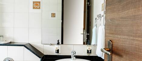 Un baño con lavamanos blanco, encimera negra y un espejo que refleja una puerta.