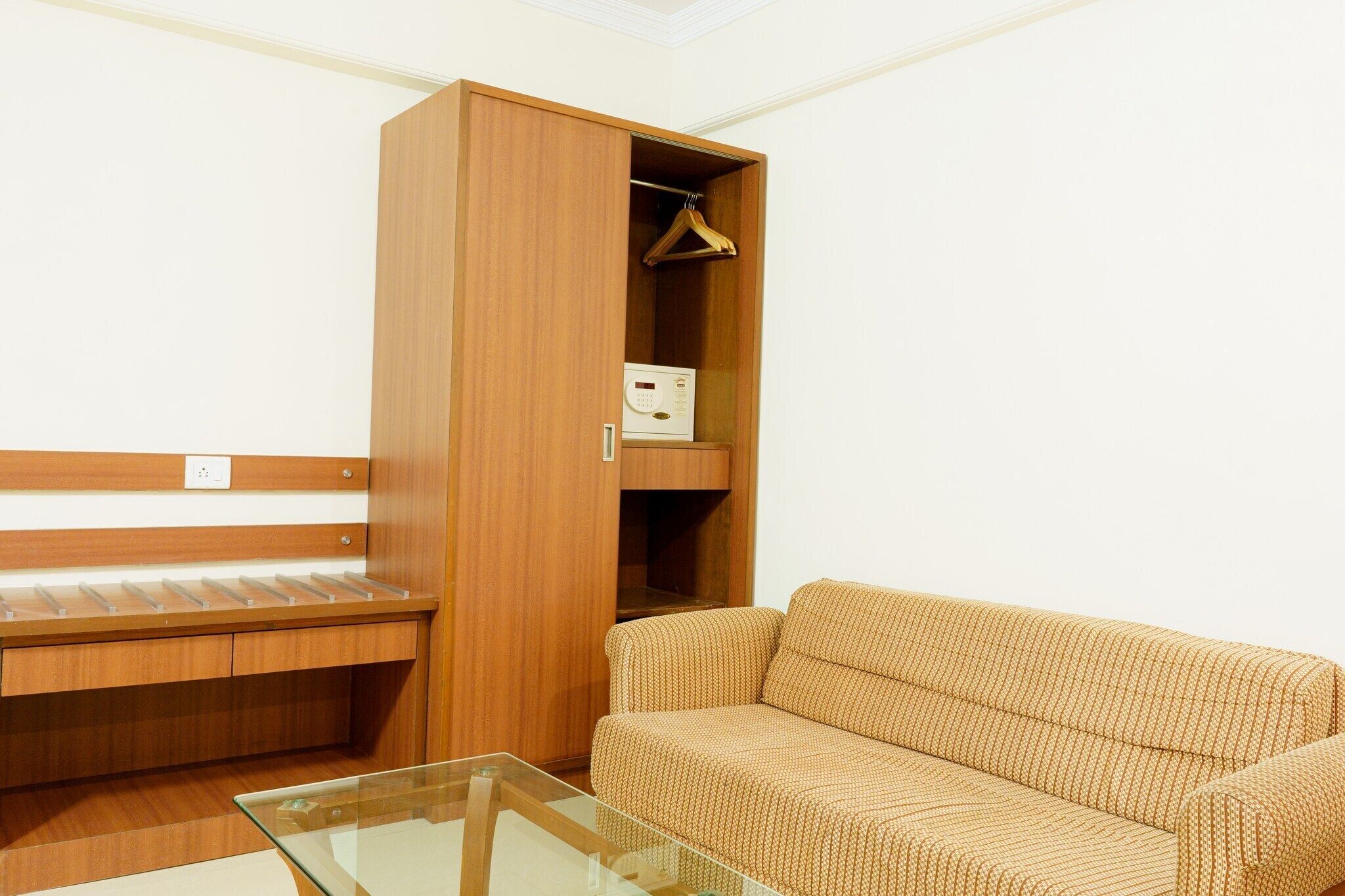 A compact room with a wooden wardrobe, a sofa, and a glass coffee table.