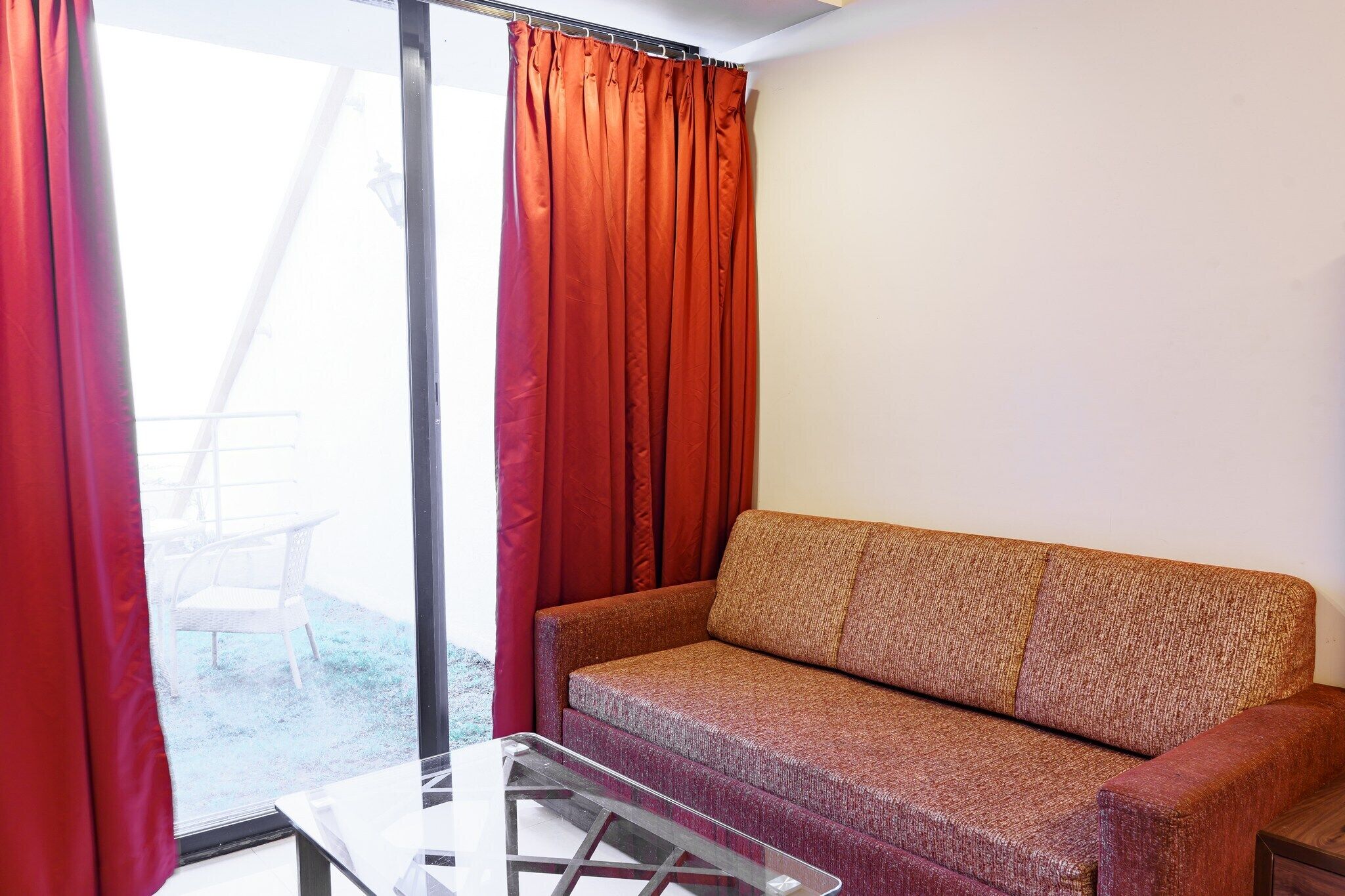 Ein Zimmer mit einer Couch, einem Glastisch und einer Schiebetür mit roten Vorhängen.