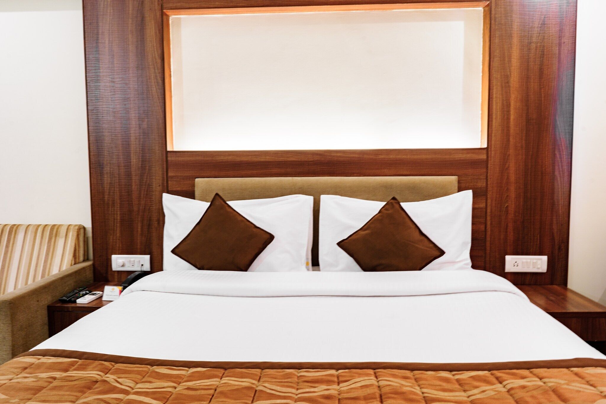 A neatly made bed with a brown headboard, white bedding, and two brown pillows.
