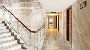 Una escalera de mármol con barandillas de vidrio que conduce a un pasillo con paredes de madera y un cartel que indica las habitaciones 201 a 214.