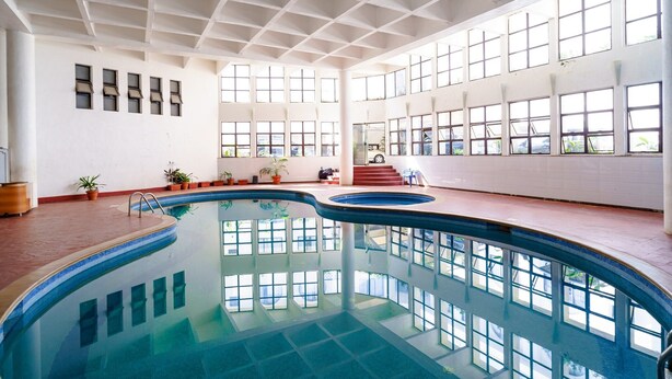 Una piscina interior con suelo de baldosas, amplias ventanas y plantas en macetas.