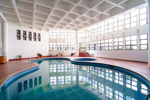 Une piscine intérieure avec un sol carrelé, de grandes fenêtres et des plantes en pot.