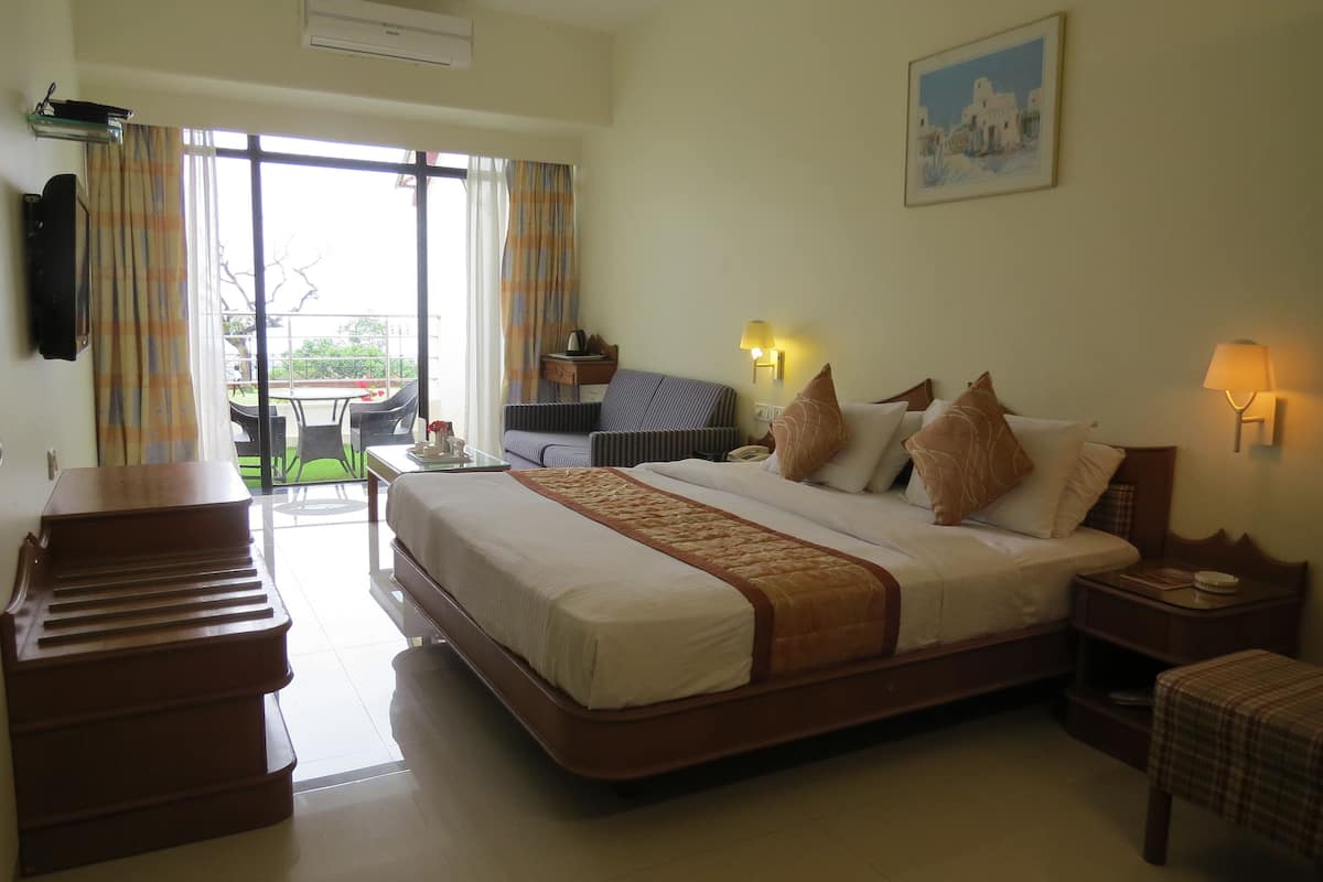A hotel room with a large bed, a desk, a chair, a small table, and a balcony with a view.