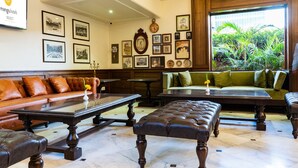 Un hall de hotel con un sofá de cuero, un sofá verde y una mesa de centro. Hay cuadros en la pared y un reloj.
