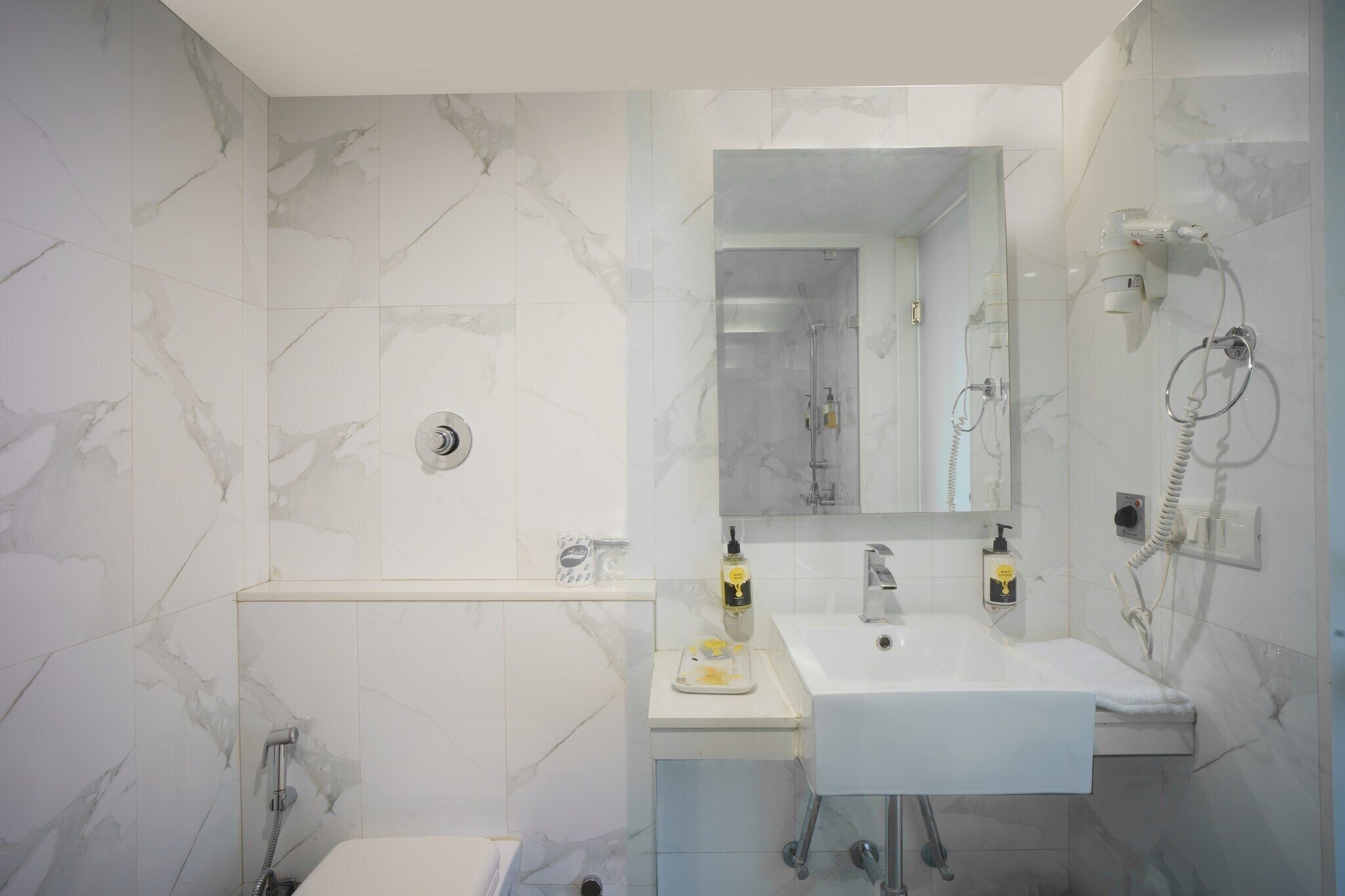 Un baño moderno con detalles de mármol, un lavamanos, un espejo y zona de ducha.