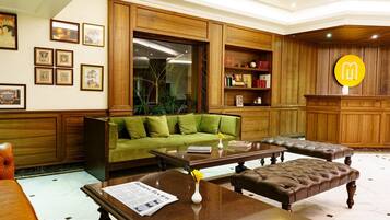 A modern living room with a green sofa, leather ottomans, a coffee table, and a wooden bookshelf.