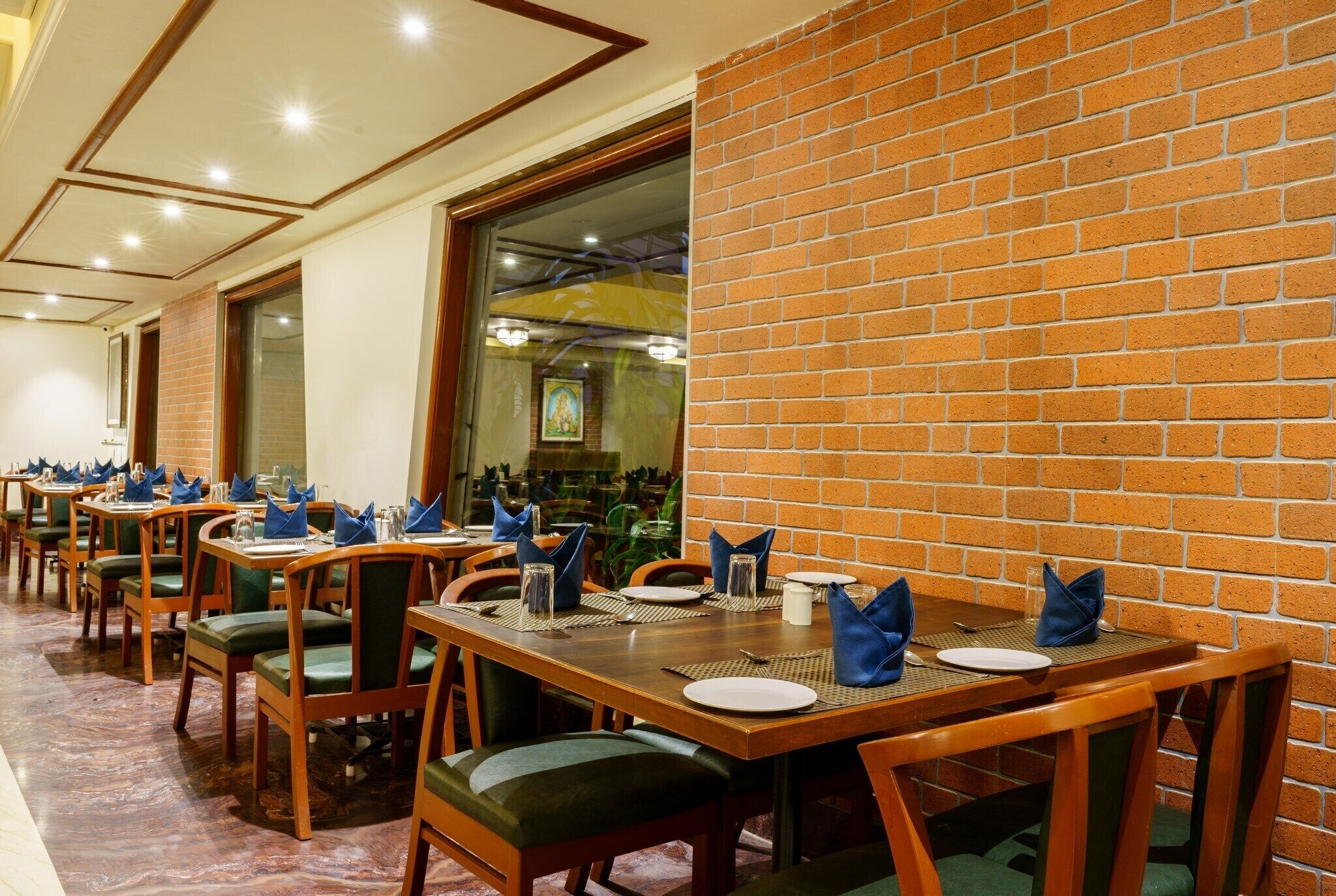 A restaurant with multiple tables set for dining, featuring green upholstered chairs and wooden tables.