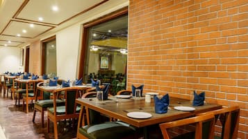 A restaurant with multiple tables set for dining, featuring green upholstered chairs and wooden tables.
