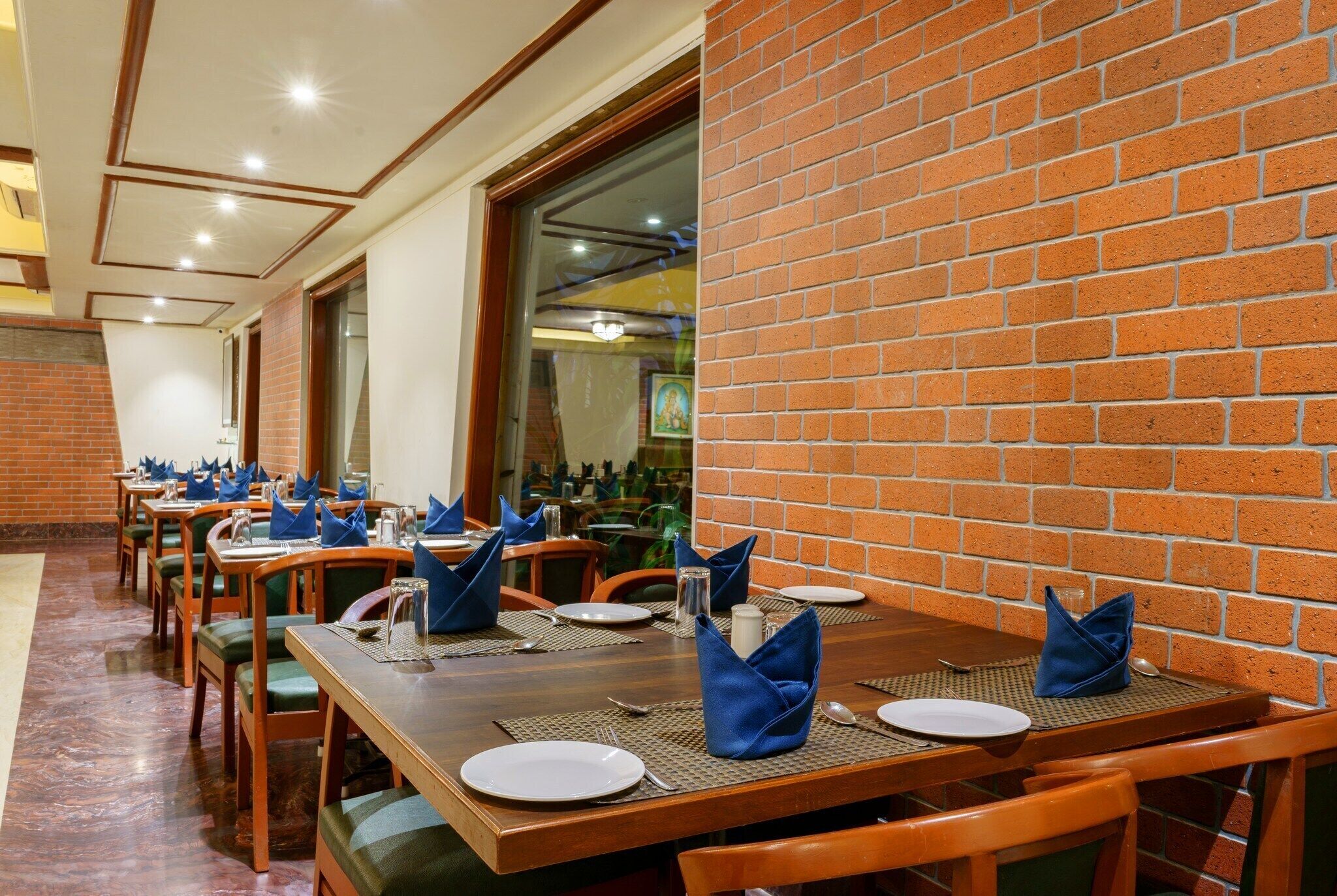Um restaurante com paredes de tijolo, mesas de madeira e cadeiras estofadas verdes.