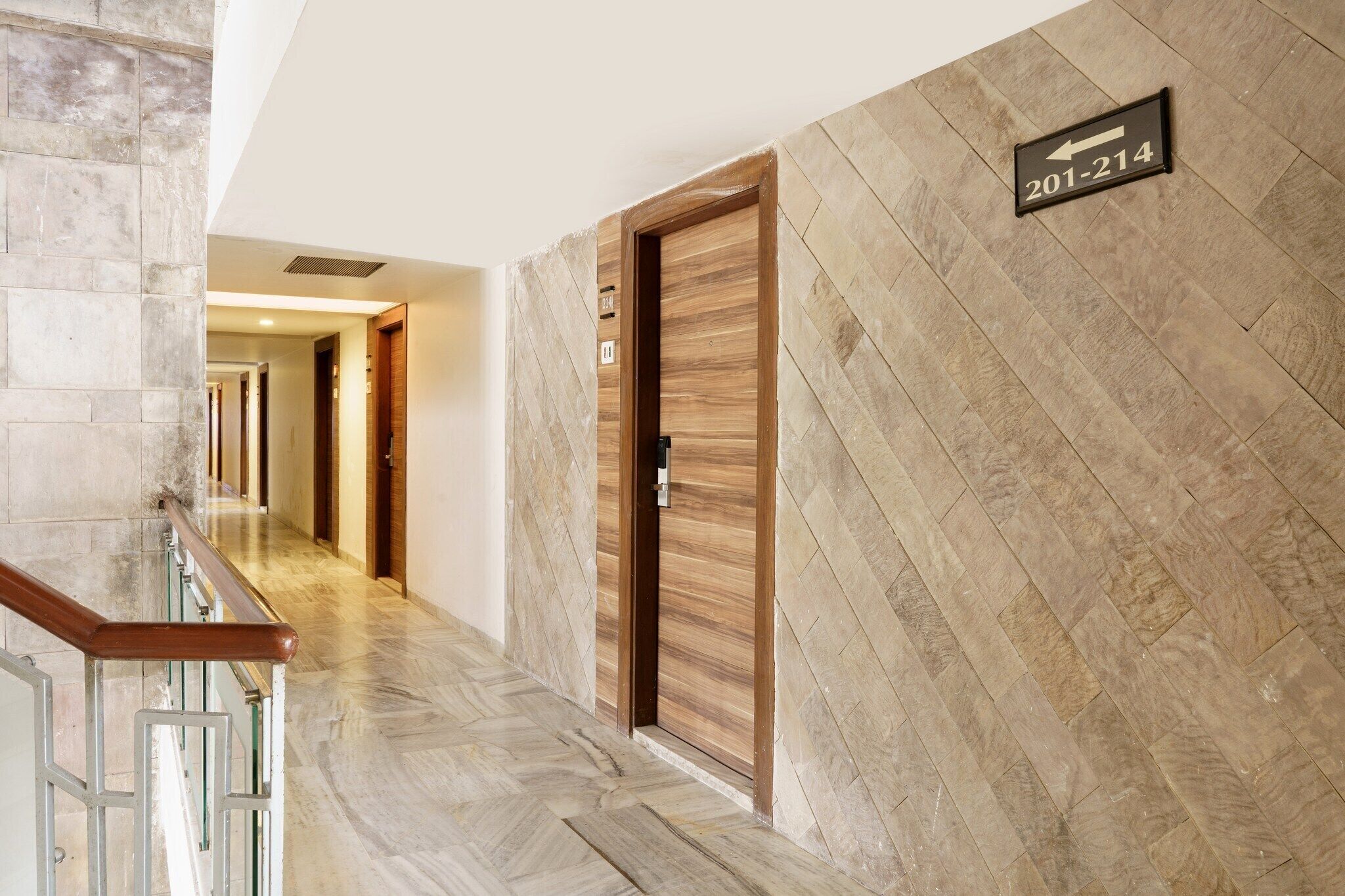 Ein Hotelkorridor mit einer Holztür, auf der 201-214 steht, einem Marmorboden und einem Metallgeländer.
