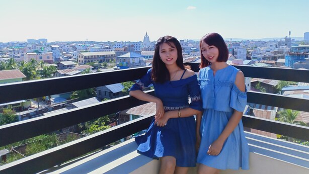Two individuals on a balcony overlooking a cityscape with buildings and a clear sky. - Hotel Duo Swan (Mandalay)