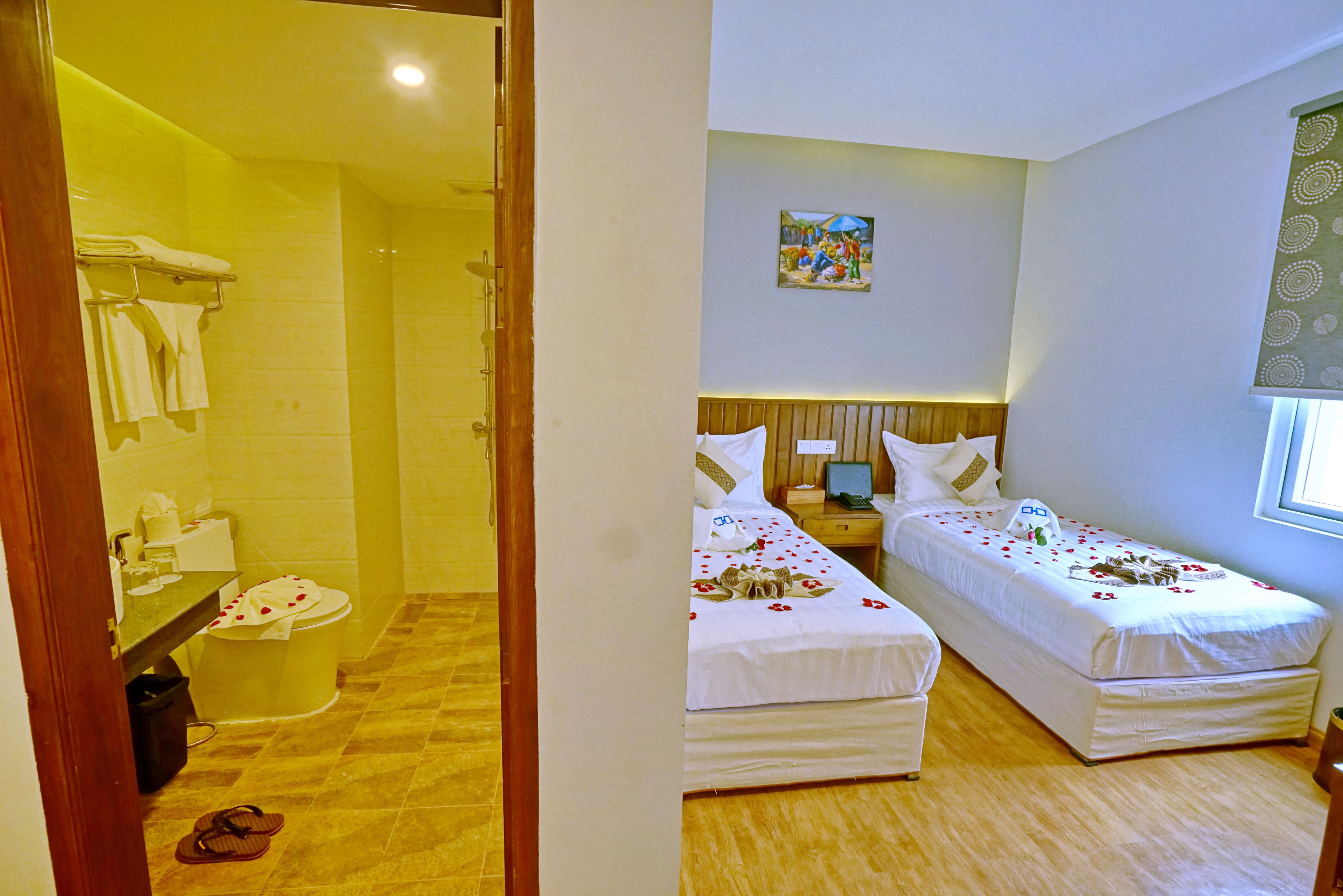 A hotel room with two single beds, a shower area, a bathroom, and a small bedside table with a lamp.
