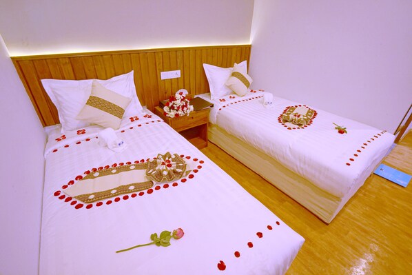 Two single beds with wooden headboards, white bedding, and decorative elements like rose petals and a mirror. - Hotel Duo Swan (Mandalay)
