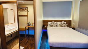 A hotel room with a wooden bed, a bedside table, a mirror, and a small desk with a kettle and cups. - Hotel Duo Swan (Mandalay)