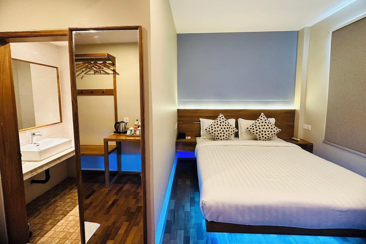 A hotel room with a wooden bed, a bedside table, a mirror, and a small desk with a kettle and cups.