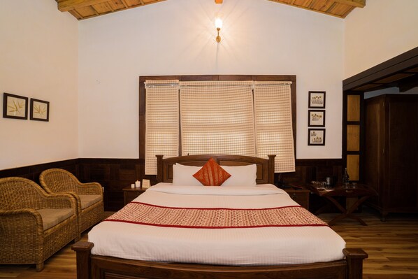 A neatly arranged bedroom with a large bed, a wooden headboard, a wicker sofa, and a window with curtains. - Bhikampur Lodge By Howard (Nainital)