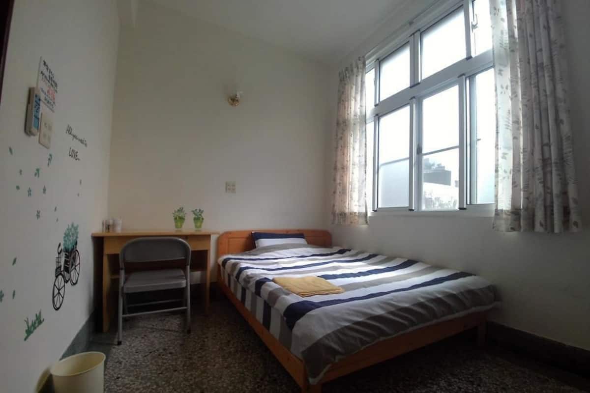 Ein kleines, ordentliches Zimmer mit einem Einzelbett, einem Schreibtisch und einem Stuhl.